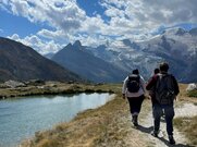 Drei Personen auf einem Wanderweg entlang einem Bergsee.